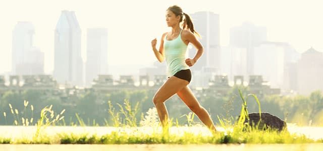 Woman running outdoors in a sunny urban park, representing exercise for addiction recovery and building physical and mental strength.