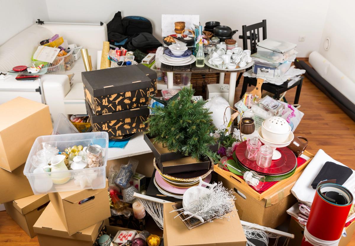 Cluttered living room filled with stacked boxes dishes decorations and household items illustrating hoarding disorder excessive clutter and difficulty organizing belongings.