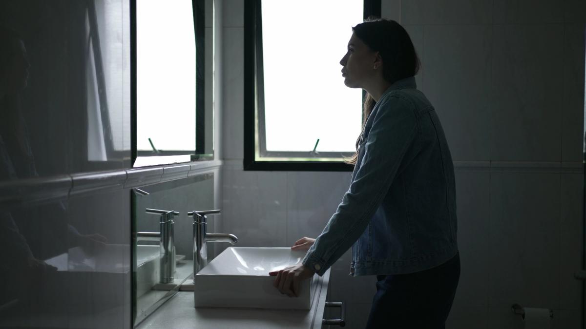 A woman standing at a bathroom sink looking distressed, symbolizing emotional and physical symptoms of Wellbutrin withdrawal.