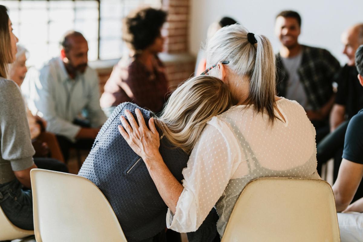 Support group members hugging and comforting another person during a recovery meeting, showing community and encouragement.