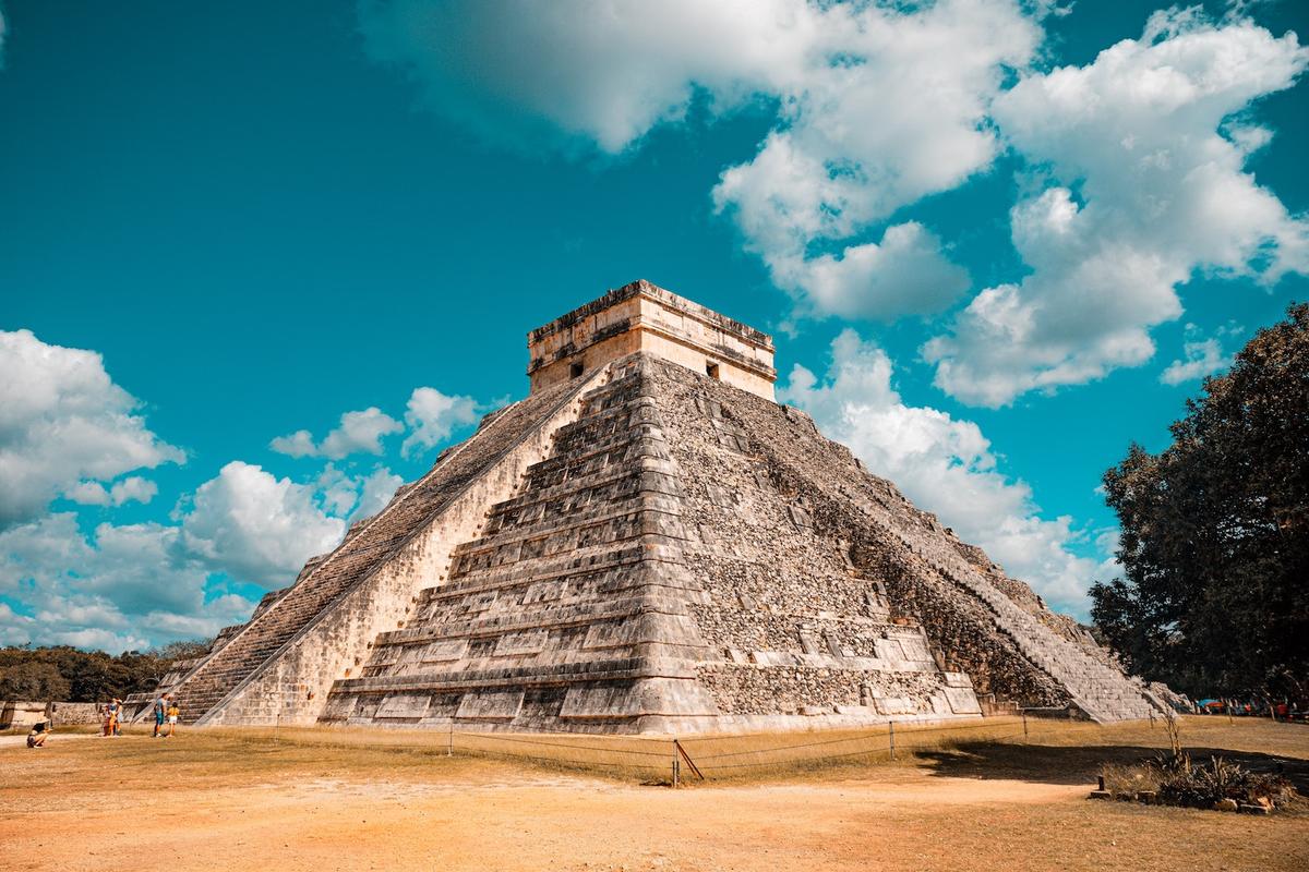 The Temple of Kukulcán (El Castillo) at Chichén Itzá under a bright blue sky with scattered white clouds.