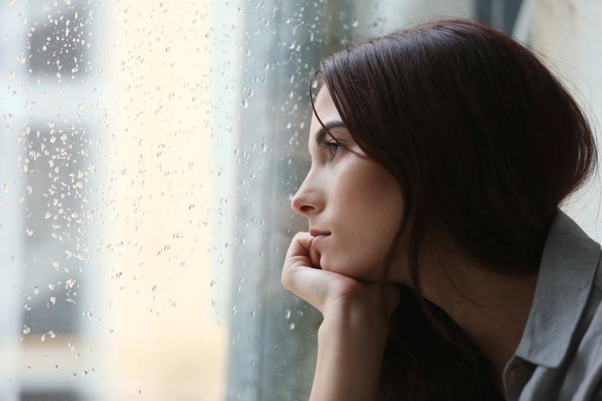 A woman looks longingly out of a window, symbolizing the need for depression treatment.