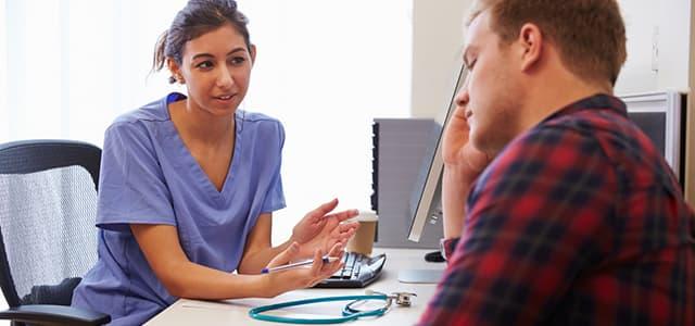 Healthcare professional speaking with a patient in an exam room as he listens with his hand on his face.