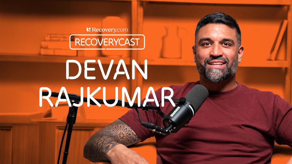 Devan Rajkumar speaking into a microphone on Recovery.com’s Recoverycast podcast, seated in a studio with an orange backdrop.