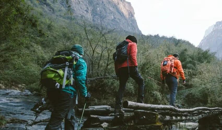 Group therapy concept of support and connection, illustrated by three hikers working together to cross a stream in a remote mountain landscape