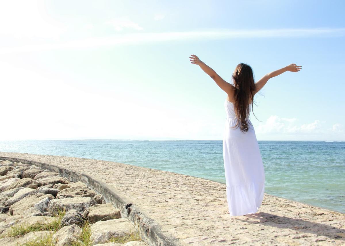 A woman standing on the beach on a sunny day with her arms outstretched. 