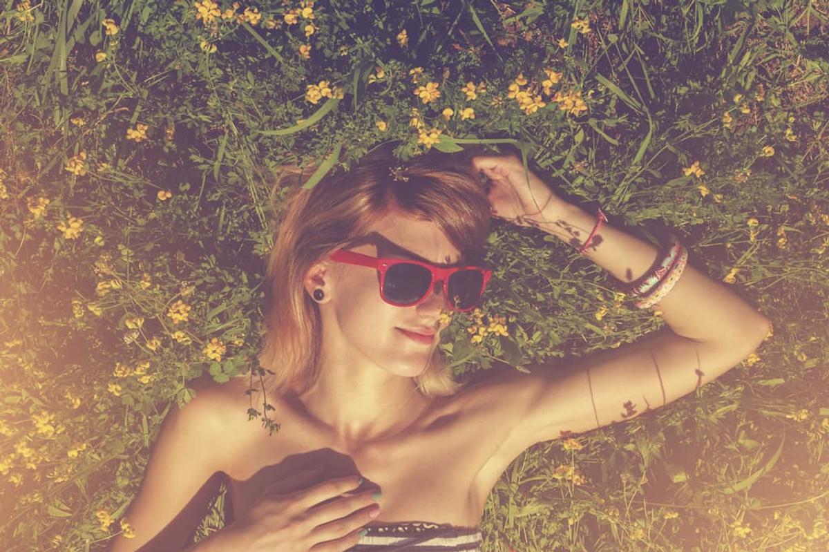 Person relaxing peacefully in field of wildflowers wearing red sunglasses