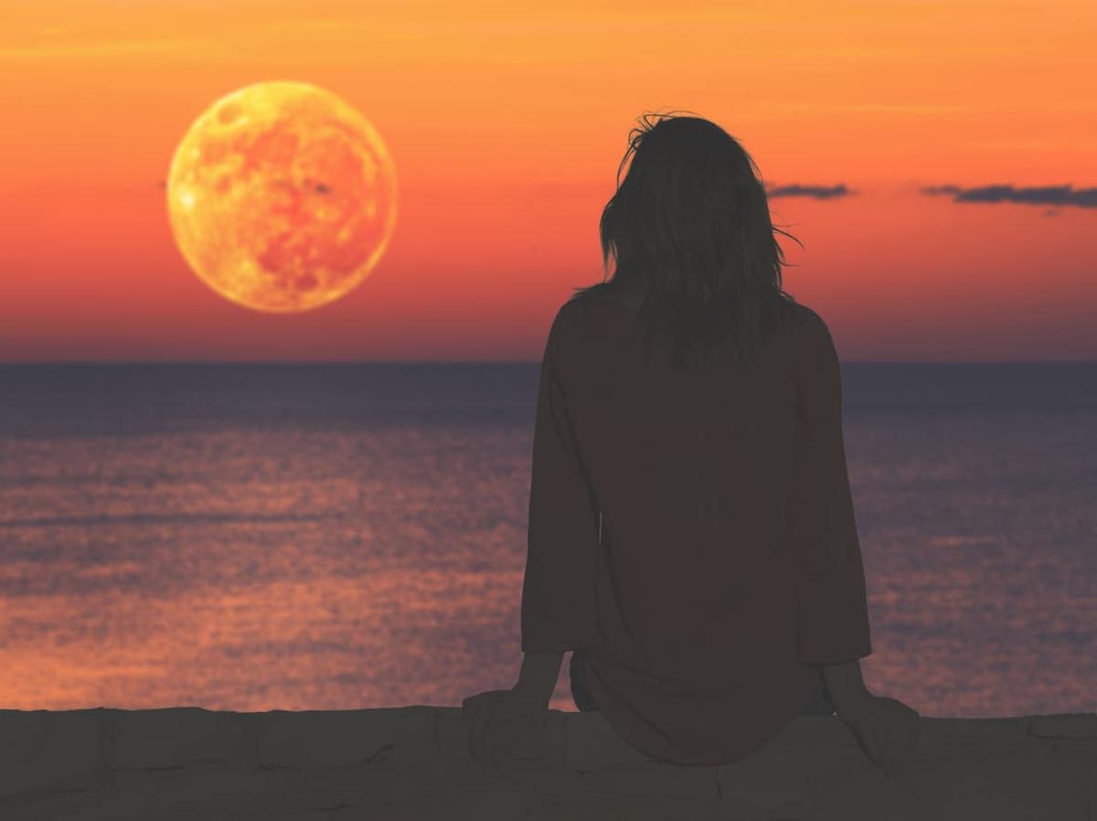 A silhouette of a person with long hair sitting and facing an ocean sunset. 