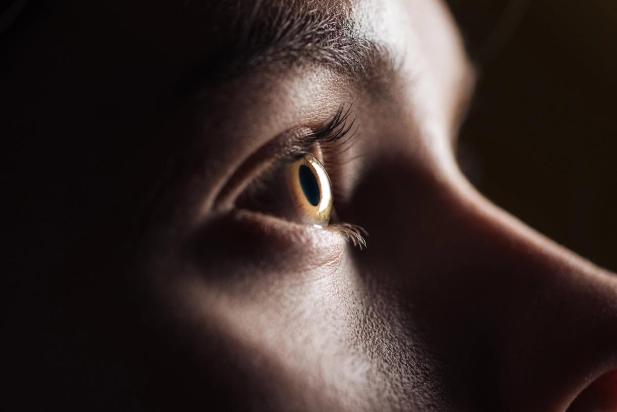 Extreme close-up of a person’s eye in low light, showing detailed eyelashes and iris, conveying focus, alertness, or intense thought.