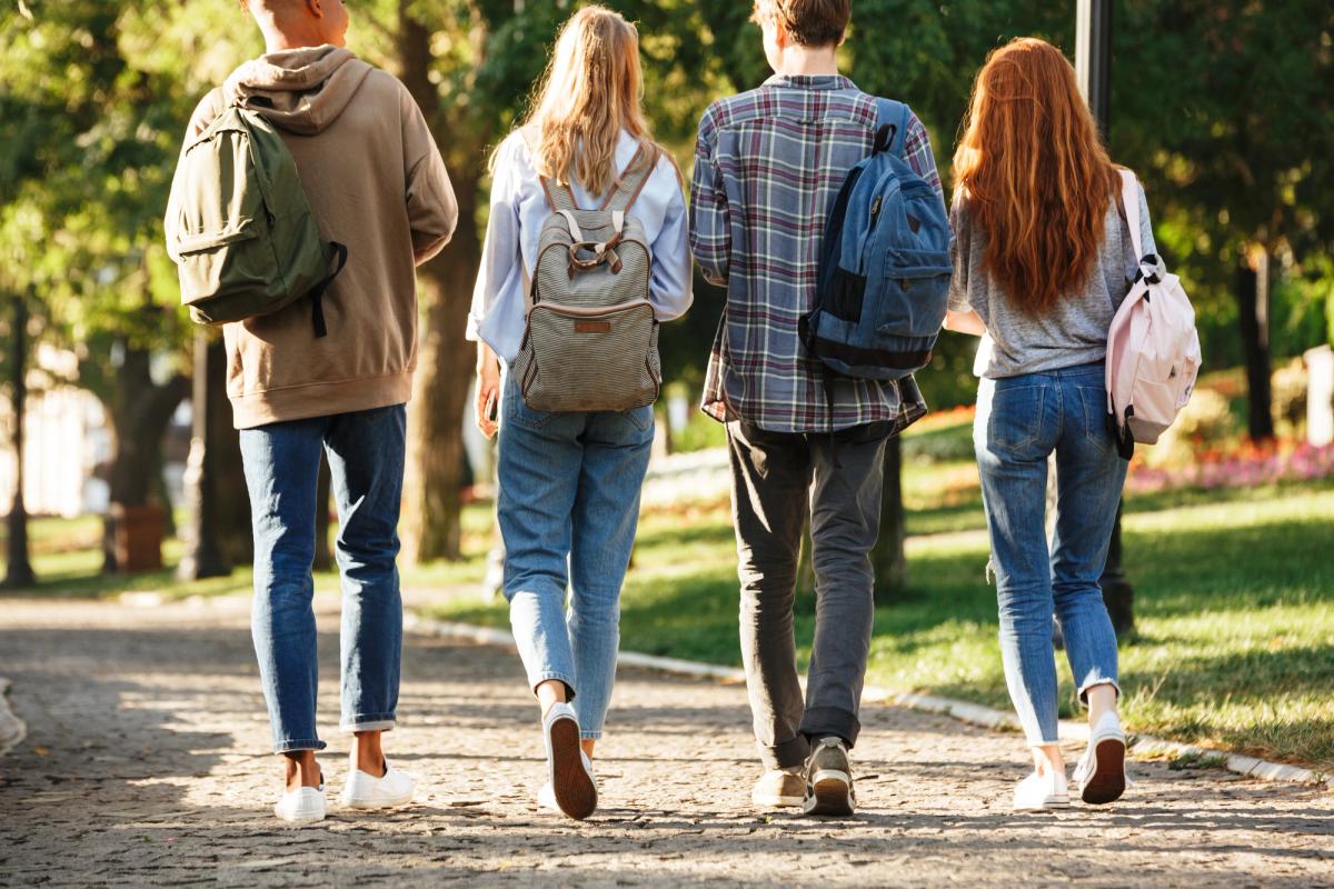 Four students with backpacks walking side by side. 