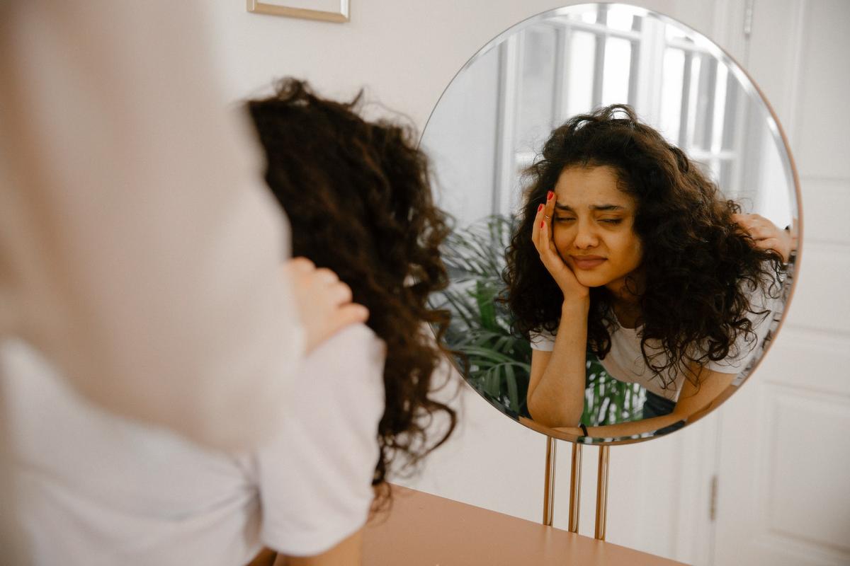 Woman with depression looking at herself in a round mirror with a concerned expression