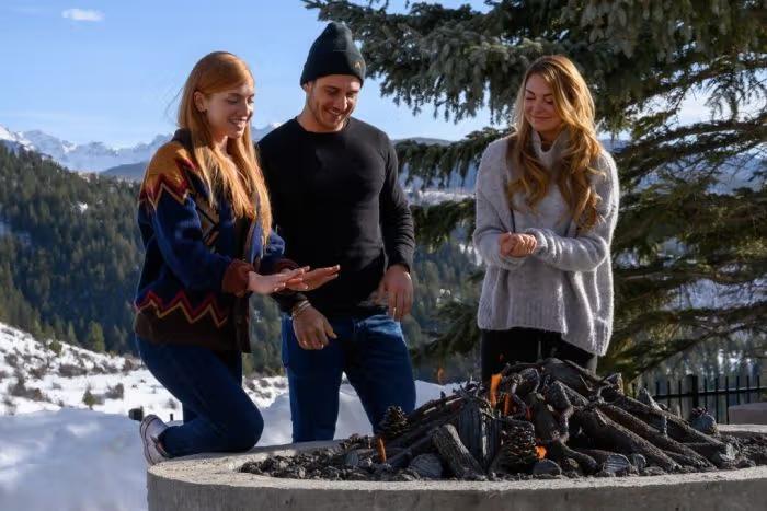 Group therapy concept of connection and support, shown by three people bonding and warming hands by a fire in a peaceful outdoor setting