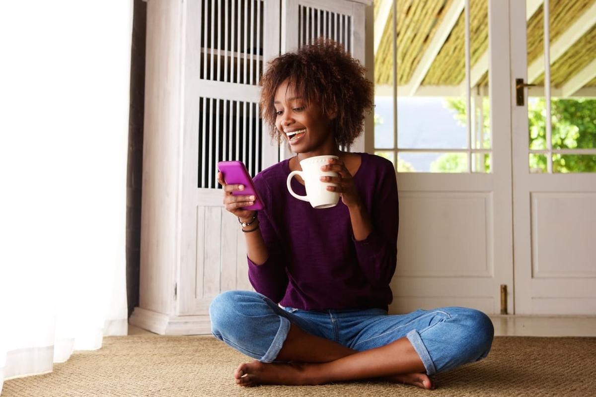 Happy woman enjoying coffee and phone at home, illustrating healthy social media use in recovery