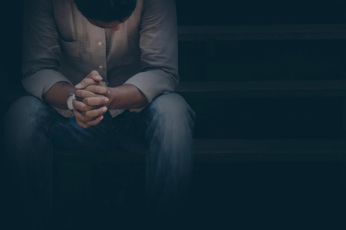 Man sitting alone on stairs with his head bowed and hands clasped, conveying feelings of sadness, stress, or emotional distress.