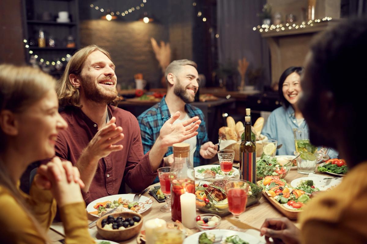 A diverse group of friends laughing and talking around a dinner table laden with food.