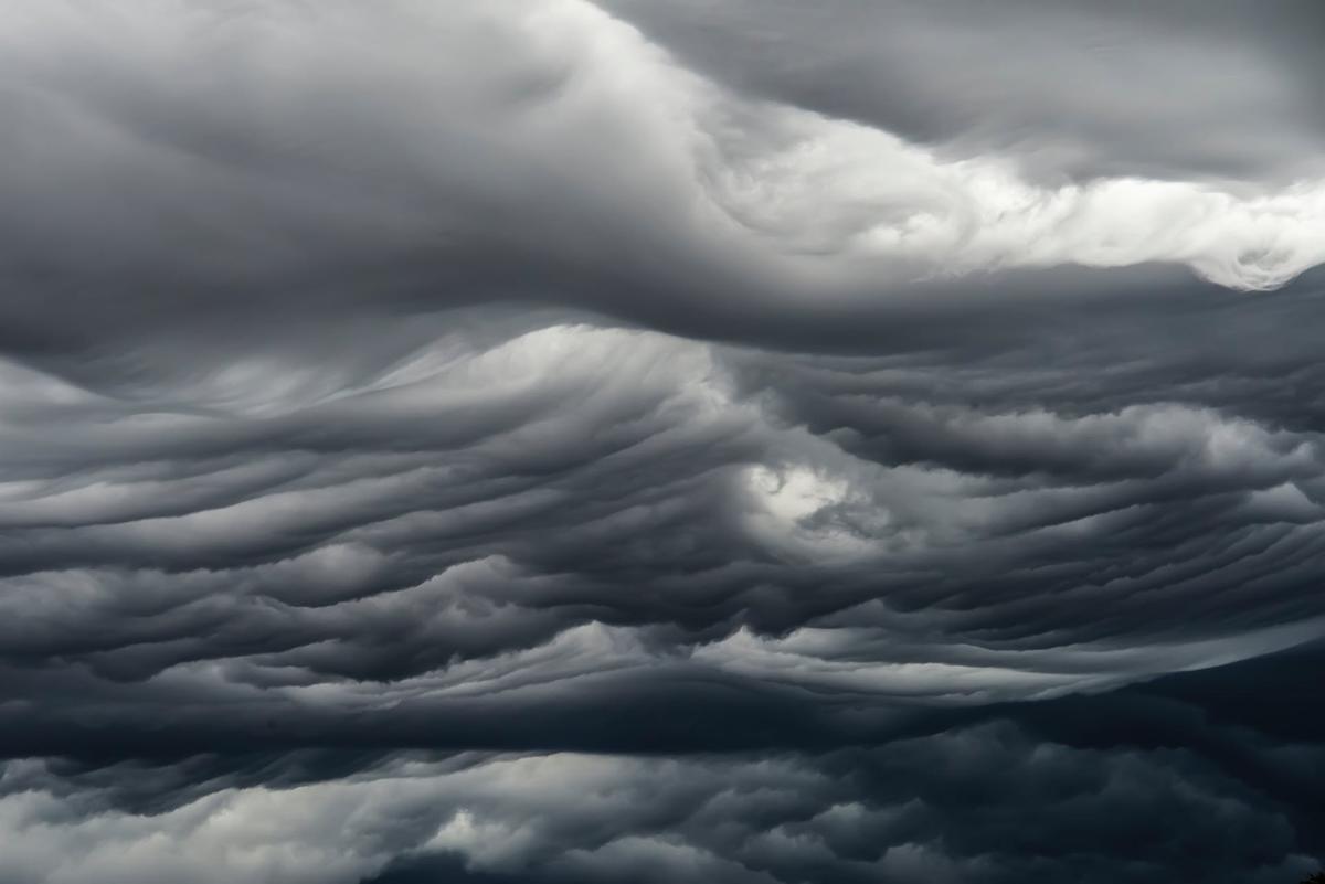 Dark, layered storm clouds swirl across the sky in shades of gray, creating a dramatic, turbulent atmosphere.