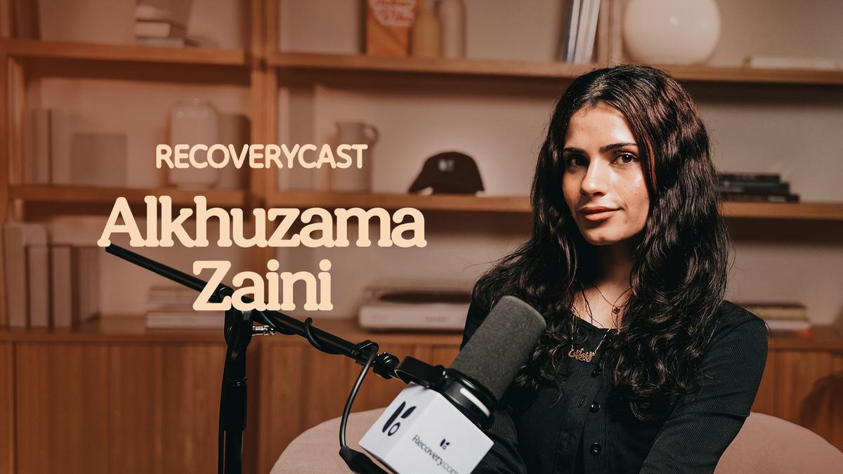 Recoverycast guest Alkhuzama Zaini sits in a podcast studio speaking into a microphone during an episode about addiction and recovery.