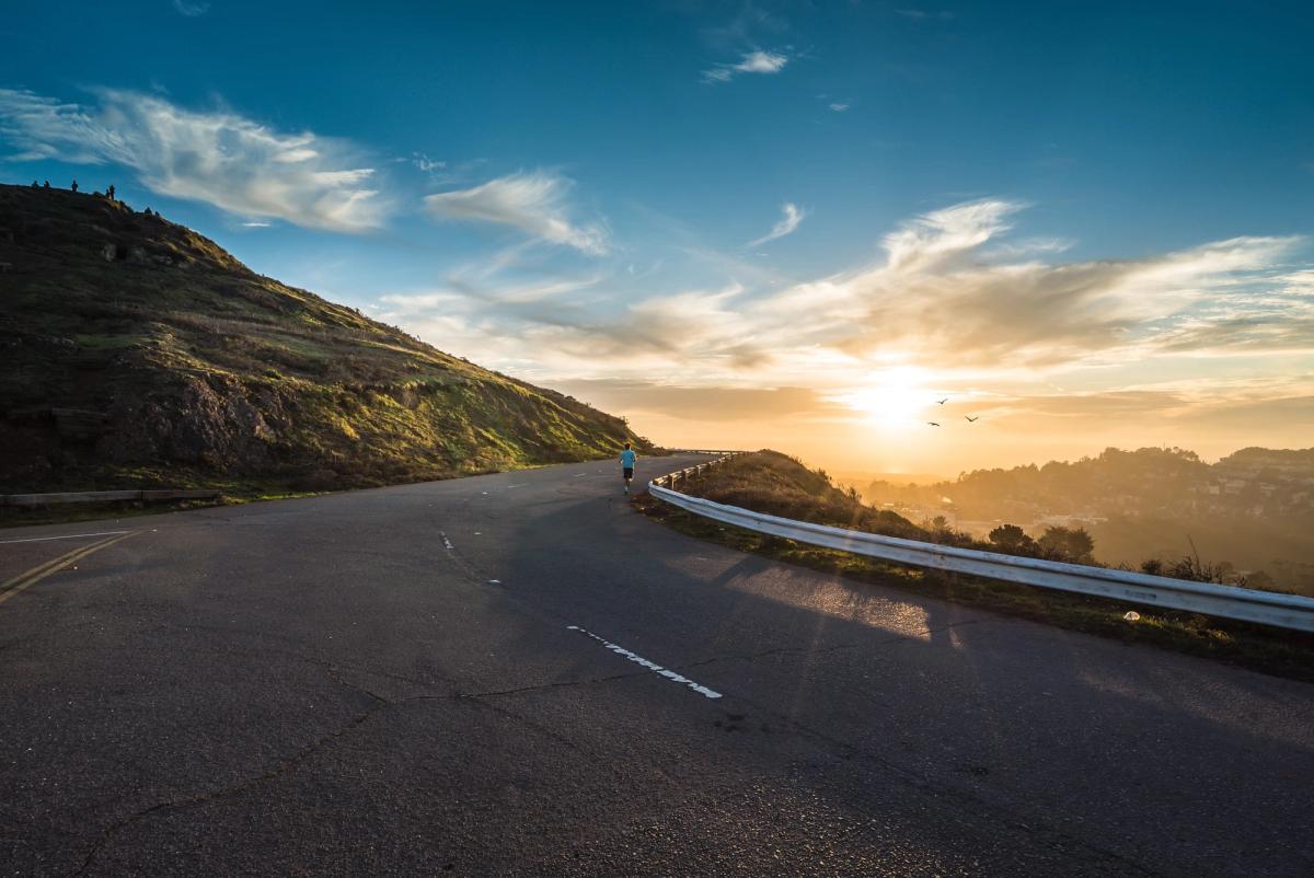 Person running along a winding mountain road at sunrise, symbolizing perseverance, hope, and the journey of personal recovery.