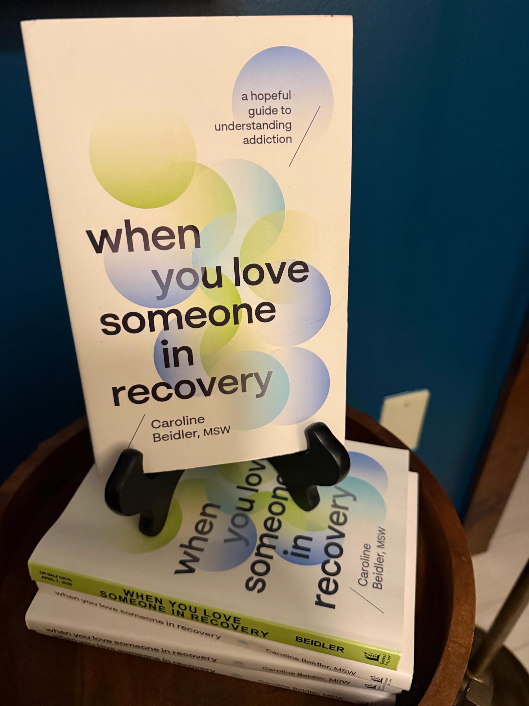 Copies of When You Love Someone in Recovery by Caroline Beidler displayed on a table with one book upright on a stand.