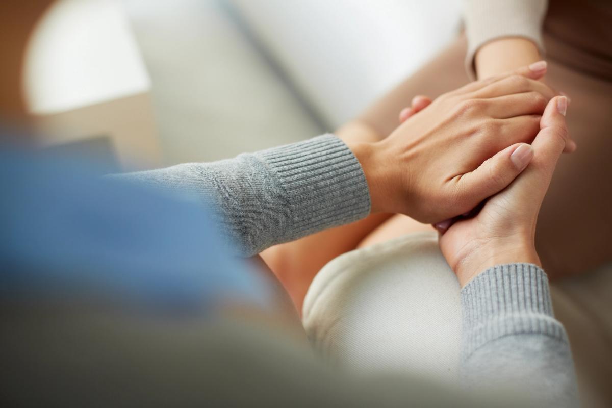 Close-up of two people holding hands in a supportive gesture, one person’s hands gently clasping the other’s, suggesting comfort and compassion.