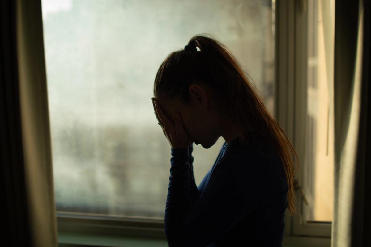 Silhouetted woman stands by a foggy window with her head bowed and face in her hands, conveying stress from struggling with cocaine and meth addiction.