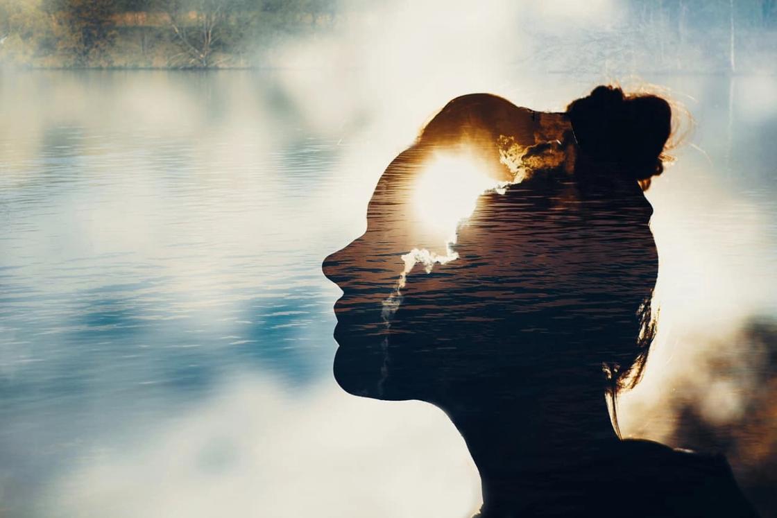 Double exposure silhouette of a woman’s profile with sunlight and calm lake water overlay, symbolizing mental health, self-reflection, and emotional healing.