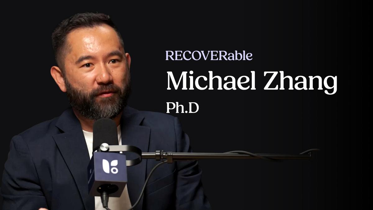 A close-up shot of Michael Zhang, Ph.D., an Asian man with short dark hair and a well-groomed beard, speaking during an interview or podcast.
