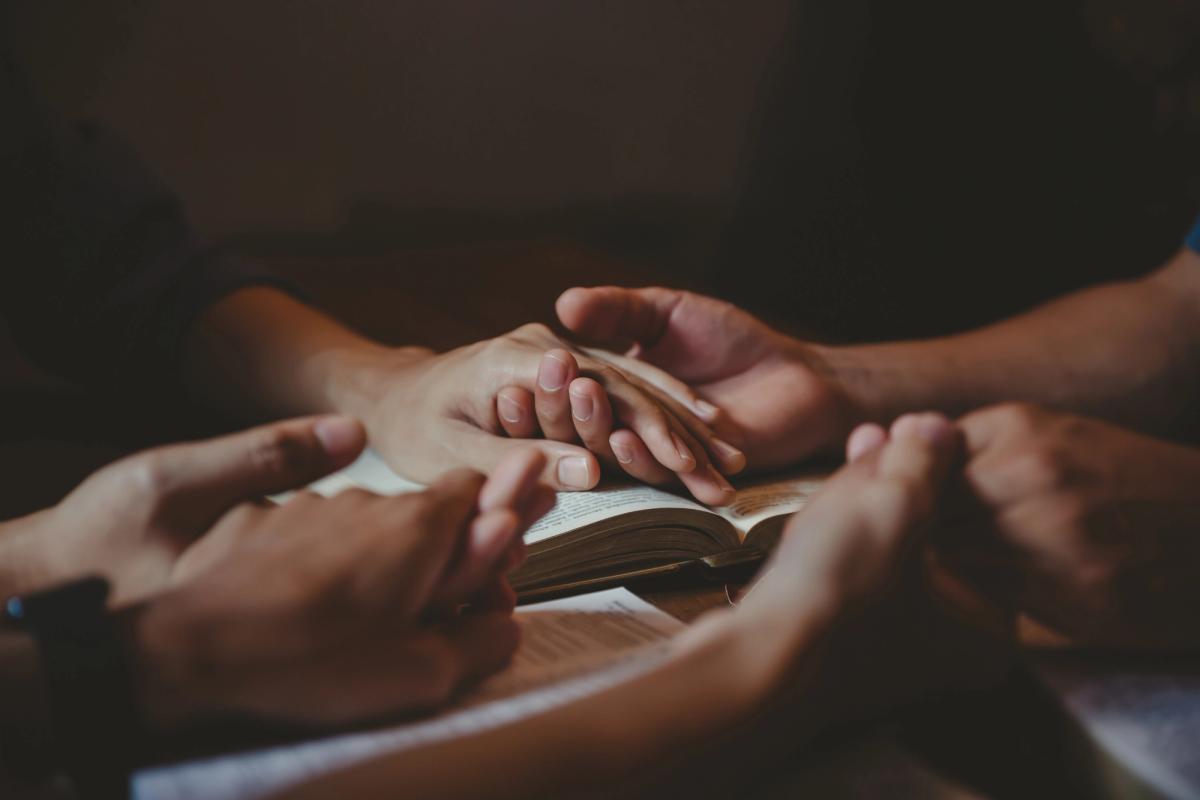 Close-up of several people holding hands in a circle over an open book.