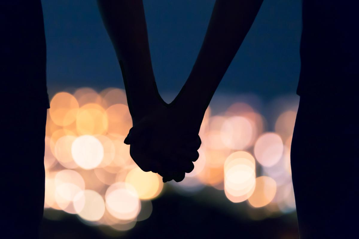 Silhouettes of two people holding hands at night with blurred city lights in the background, symbolizing relationship dependence.