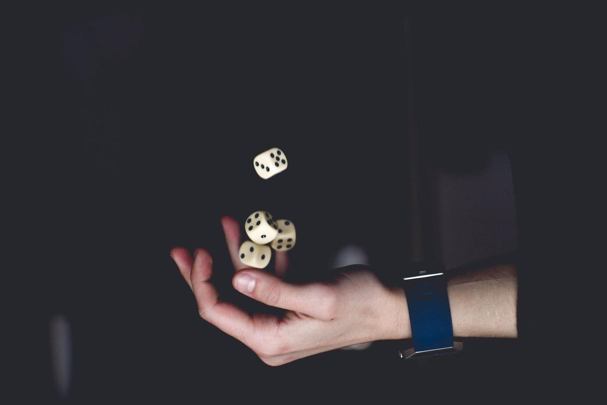Close-up of a hand tossing several white dice in the air against a dark background.