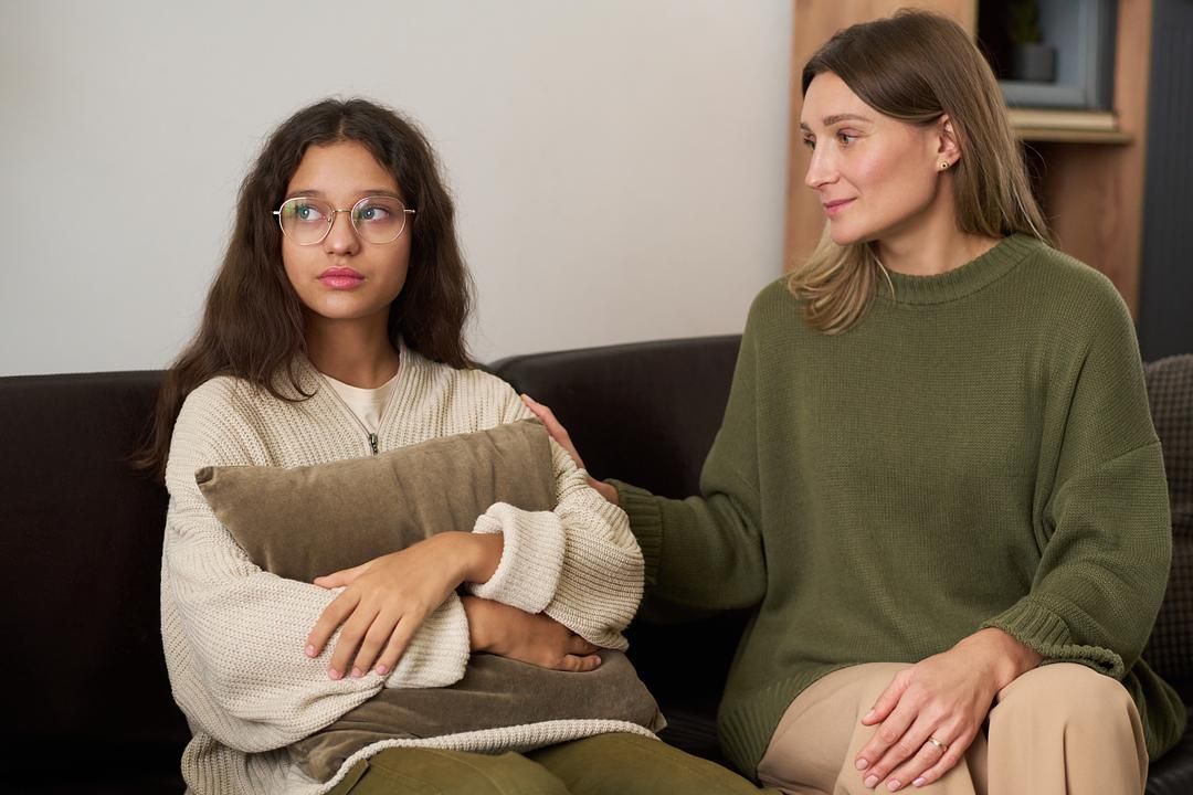 Concerned teenage girl sitting with a supportive mother during an emotional conversation at home