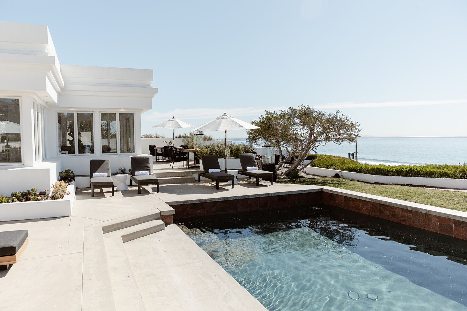 A bright, modern white villa features an outdoor patio with a dark-bottomed swimming pool.