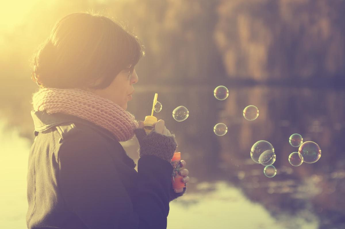 Woman in winter clothing blowing soap bubbles outside, with soft golden light suggesting hope and new beginnings