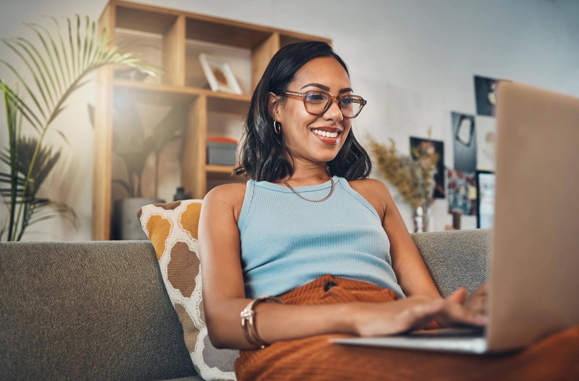Smiling woman using a laptop while relaxing on a couch at home.