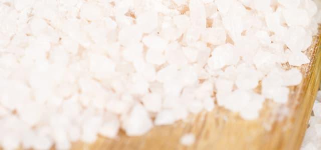 A close-up, high-angle view of coarse white sea salt crystals piled on a wooden surface