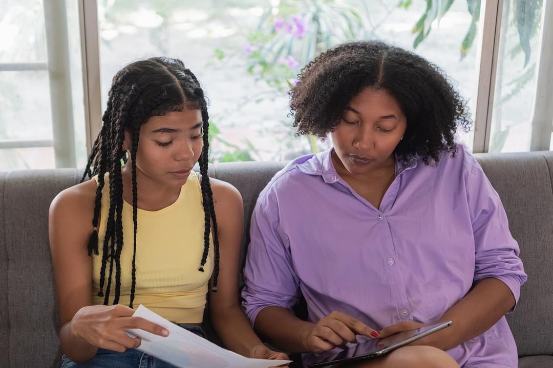 Mother and teenage daughter reviewing paperwork and using a tablet together at home