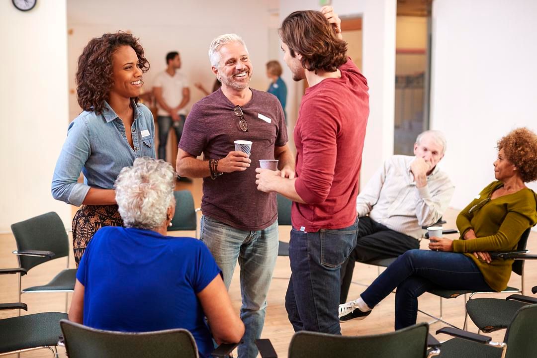 People in a recovery support group talking and connecting during a therapeutic community meeting in a rehab setting.