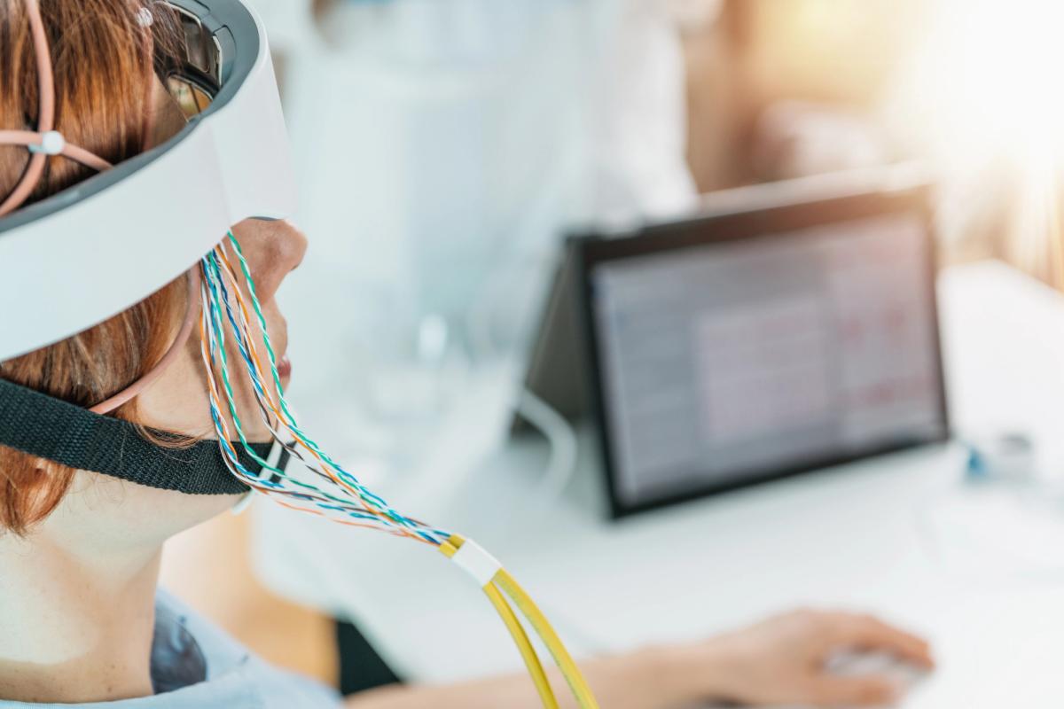 Person wearing an EEG headband with electrodes during a neurofeedback therapy session for addiction treatment, monitoring brain activity on a computer screen