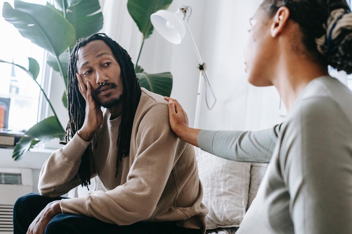 A supportive therapy setting where one person listens with concern while another rests their hand on their shoulder, representing compassionate treatment for co-occurring mental health and substance use disorders.
