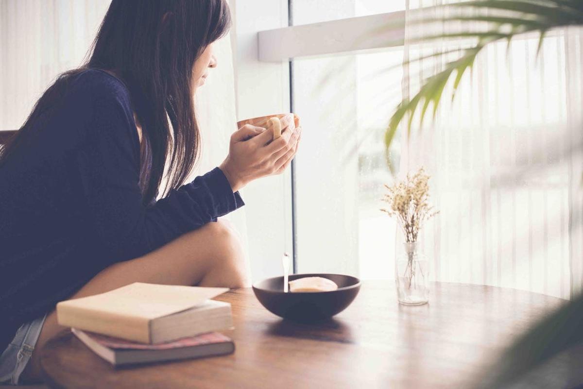 A woman sitting in a serene room, looking out the window. 