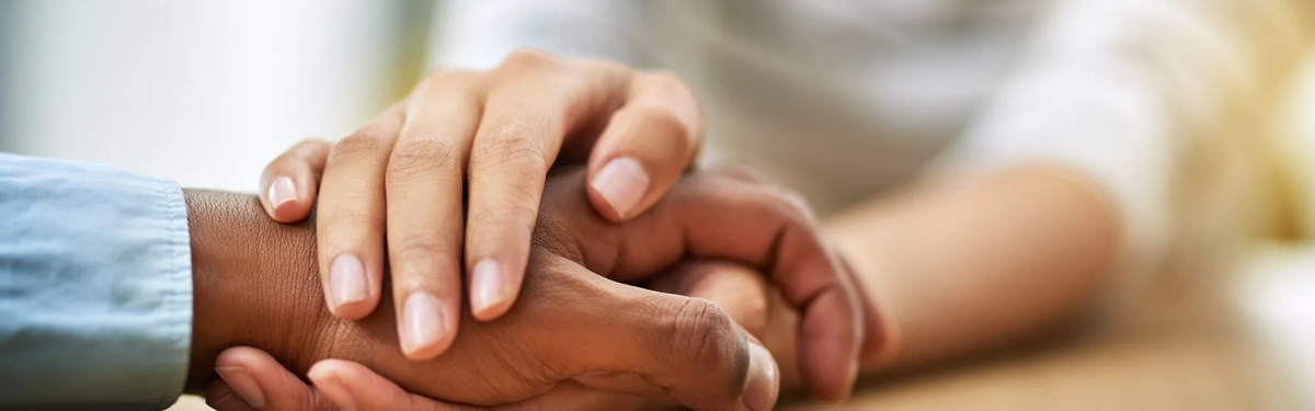 Close-up of two people holding hands in a supportive gesture, symbolizing compassion, connection, and encouragement in recovery.