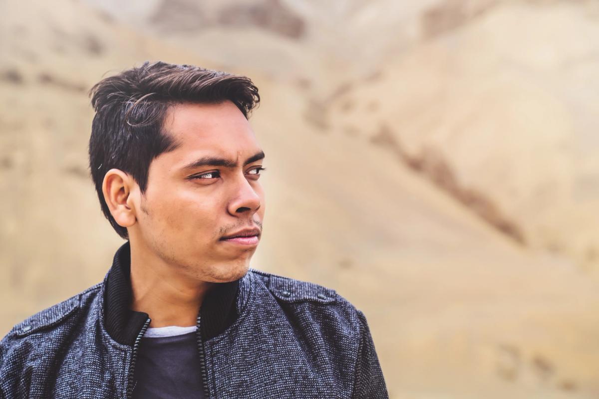 A young man standing outdoors against a sandy, desert-like landscape, looking thoughtfully into the distance, illustrating reflection and awareness around the idea that alcohol is considered a drug.