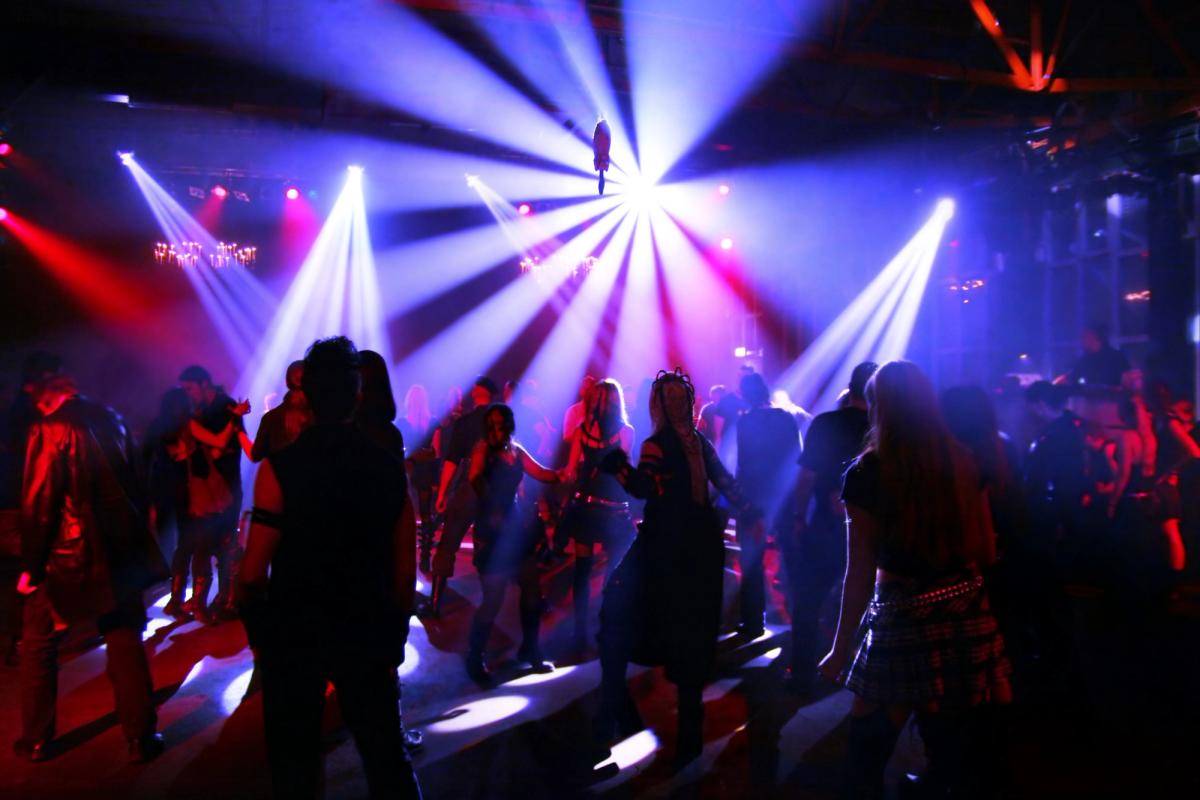 Crowd dancing on a nightclub dance floor under colorful stage lights and beams creating a vibrant nightlife atmosphere.