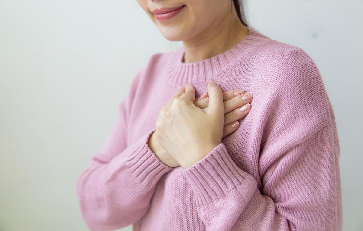 A woman wearing a pink sweater with her hands crossed over her heart, smiling gently