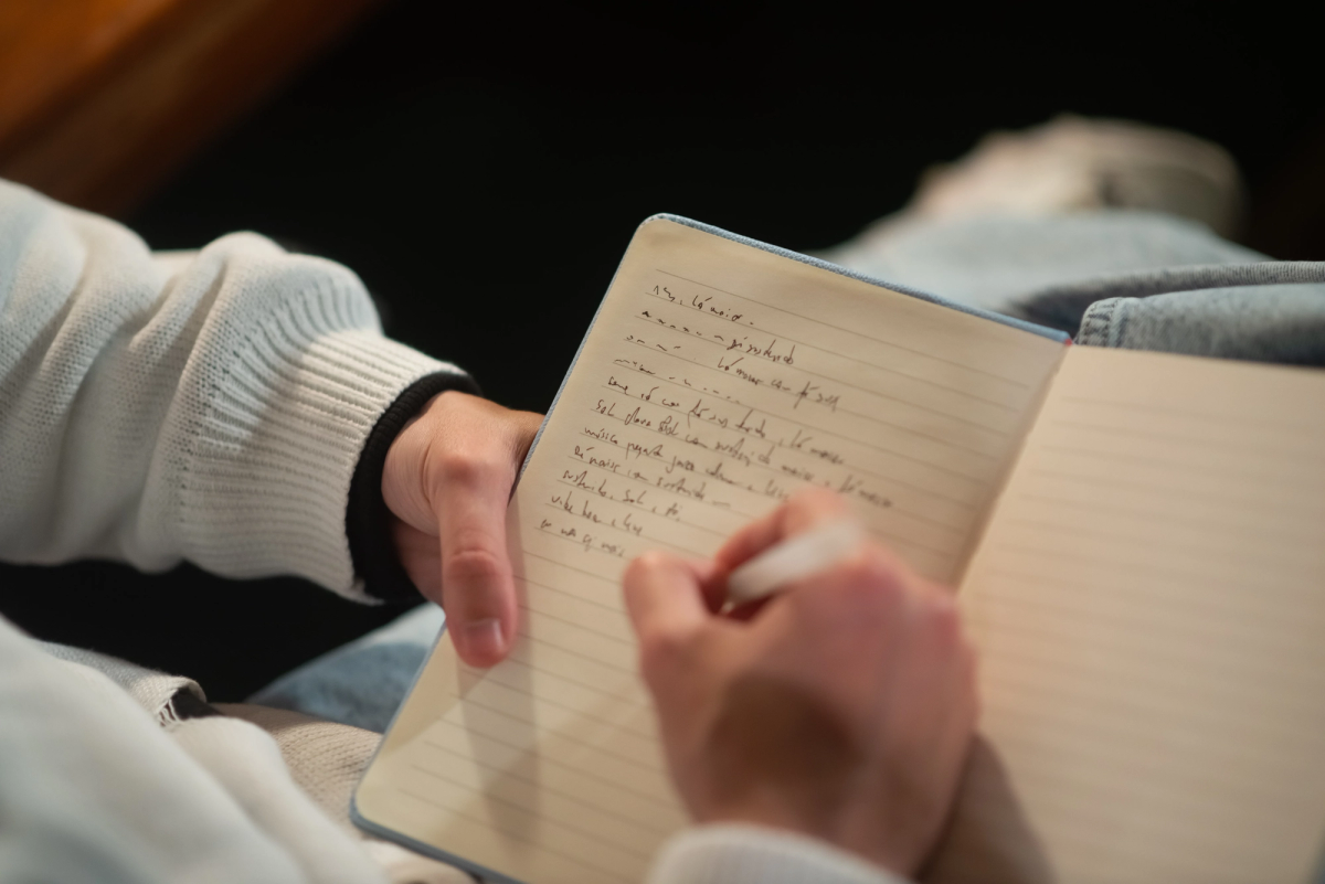 Person writing notes in an open journal with a pen, wearing a light sweater and jeans, symbolizing reflection, journaling, and personal growth.