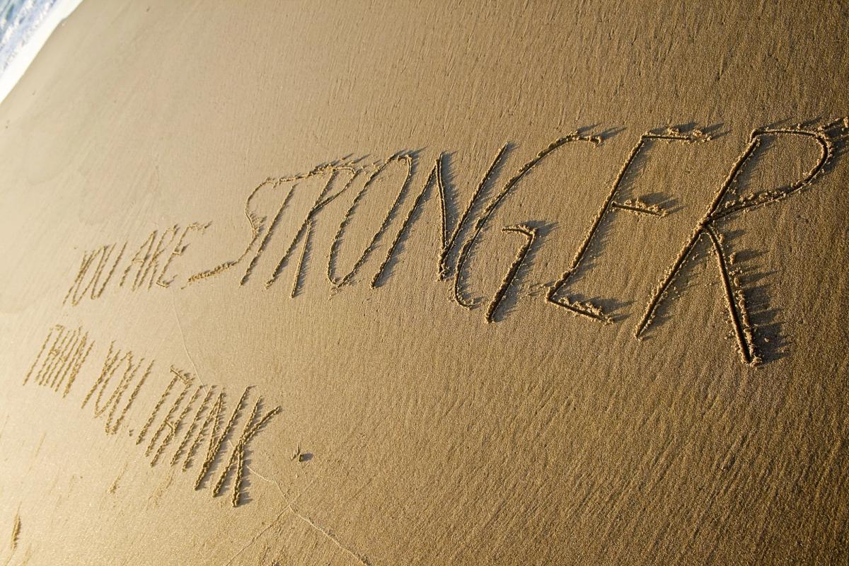 An inspirational message written in the sand on a beach that reads, "YOU ARE STRONGER THAN YOU THINK." The word "STRONGER" is written in larger, bold capital letters.