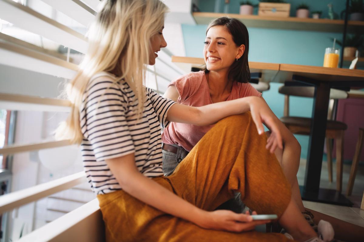 Two young women sitting on a staircase talking and smiling, representing defining success in recovery through supportive relationships, connection, and everyday progress.