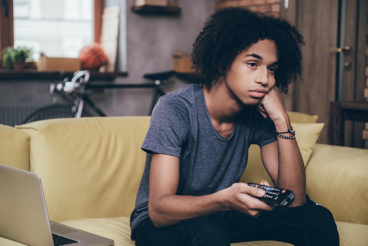 Person at home looking contemplative while holding TV remote, symbolizing the challenges of adjusting to daily life after completing addiction treatment