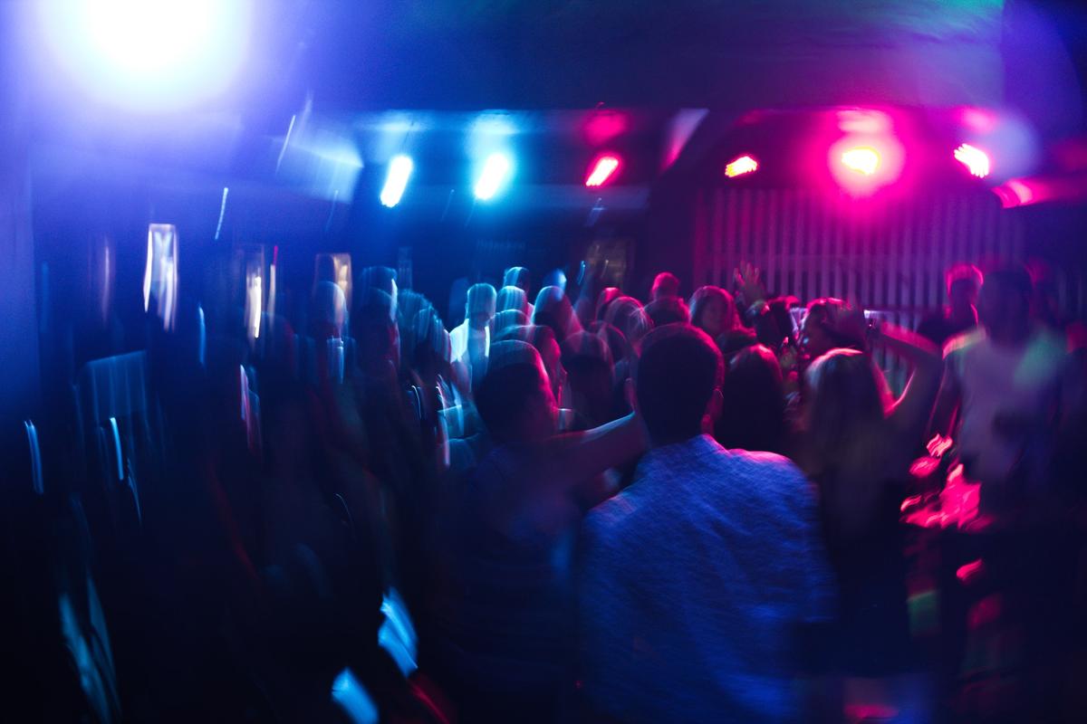 A vibrant, slightly blurred long-exposure photograph of a crowded dance floor in a dark nightclub.