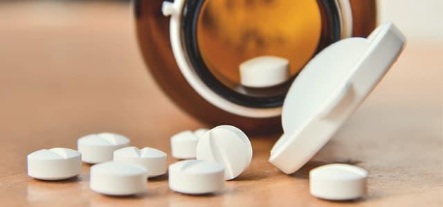 White prescription pills spilling from amber bottle, representing the risks of prescription opioid misuse and hydromorphone addiction